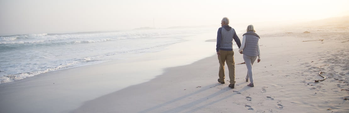 Rearview of retired couple walking on the beach.